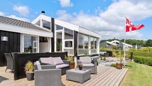 Une maison moderne dotée d’une terrasse, de mobilier d’extérieur et d’un drapeau.