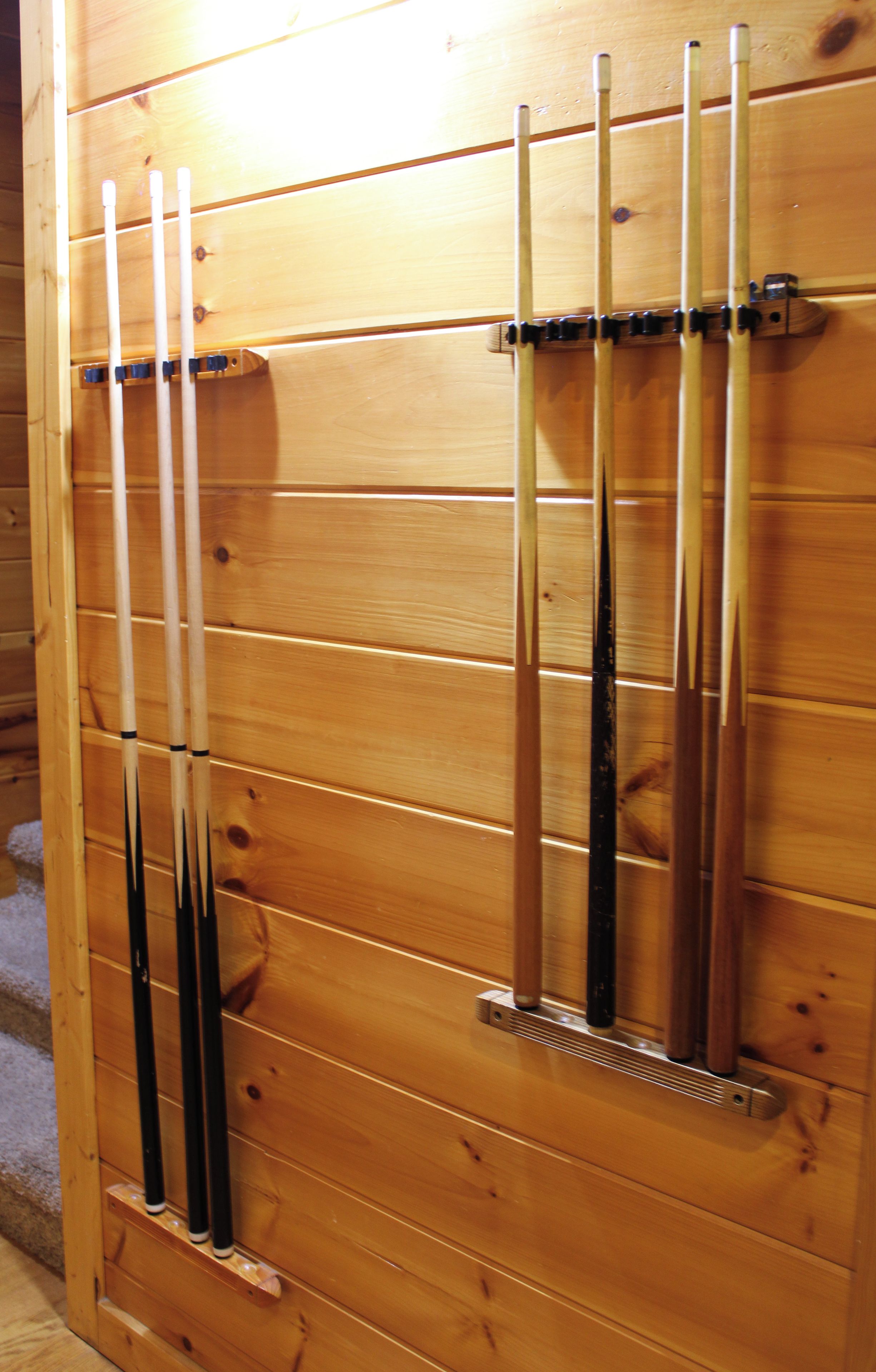 A wooden wall with multiple vertical slats, each holding a pool cue.