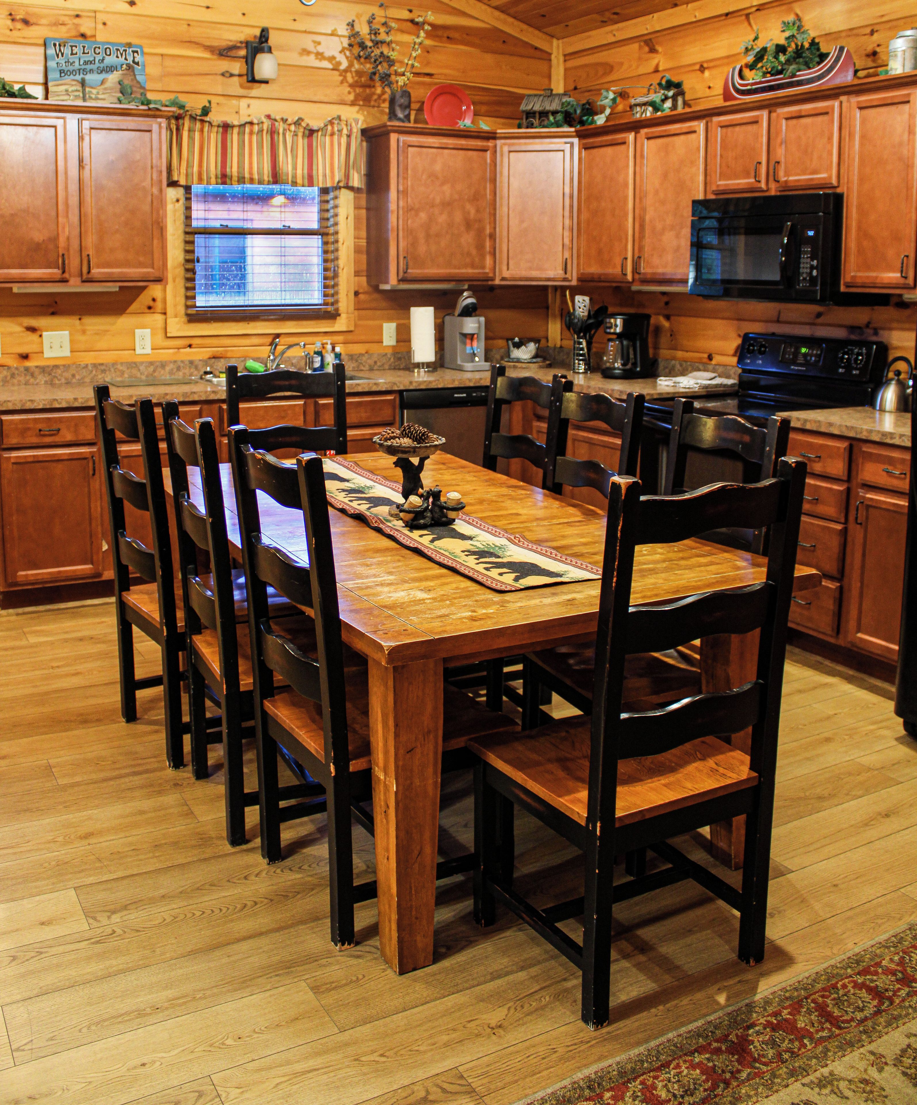 Una mesa de comedor de madera con sillas, una cocina con armarios de madera, un microondas y una cafetera.