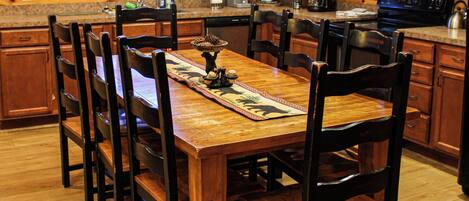 Una mesa de comedor de madera con sillas, una cocina con armarios de madera, un microondas y una cafetera.