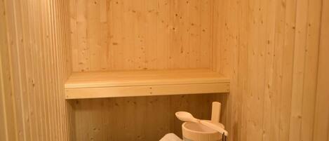 Una sauna de madera con un banco, una toalla y un cubo.