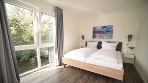 A modern bedroom with a large window, a bed, and a painting on the wall. - Familienferienhaus Mare Frisium, Meerblick, am Deich, Waschtrockner, Sauna, Ofen (Wangerland)