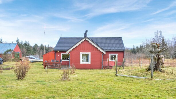 Une maison rouge avec un toit sombre, un petit porche avec des chaises et une cour clôturée.