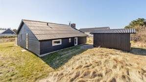 A small, dark wooden house with a sloped roof and a small attached shed. - Lovely home in Thisted with WiFi (Thisted)