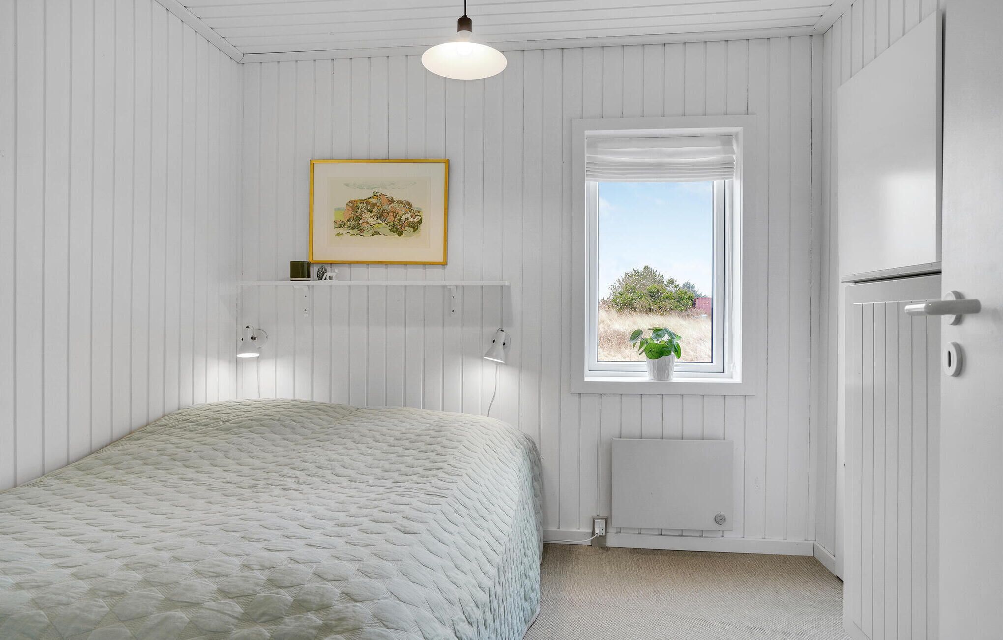 Ein Schlafzimmer mit Bett, Heizkörper, Fenster mit Aussicht und einem gerahmten Bild an der Wand.