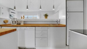 A modern kitchen with white cabinetry, wooden countertops, a built-in dishwasher, and pendant lighting. - Lovely home in Thisted with WiFi (Thisted)