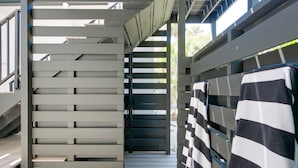 Un escalier en bois mène à un espace extérieur abrité où une serviette à rayures est suspendue à un porte-serviettes.