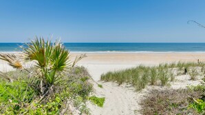 Une plage avec un ciel dégagé, un sentier sablonneux menant à l’eau et quelques plantes.