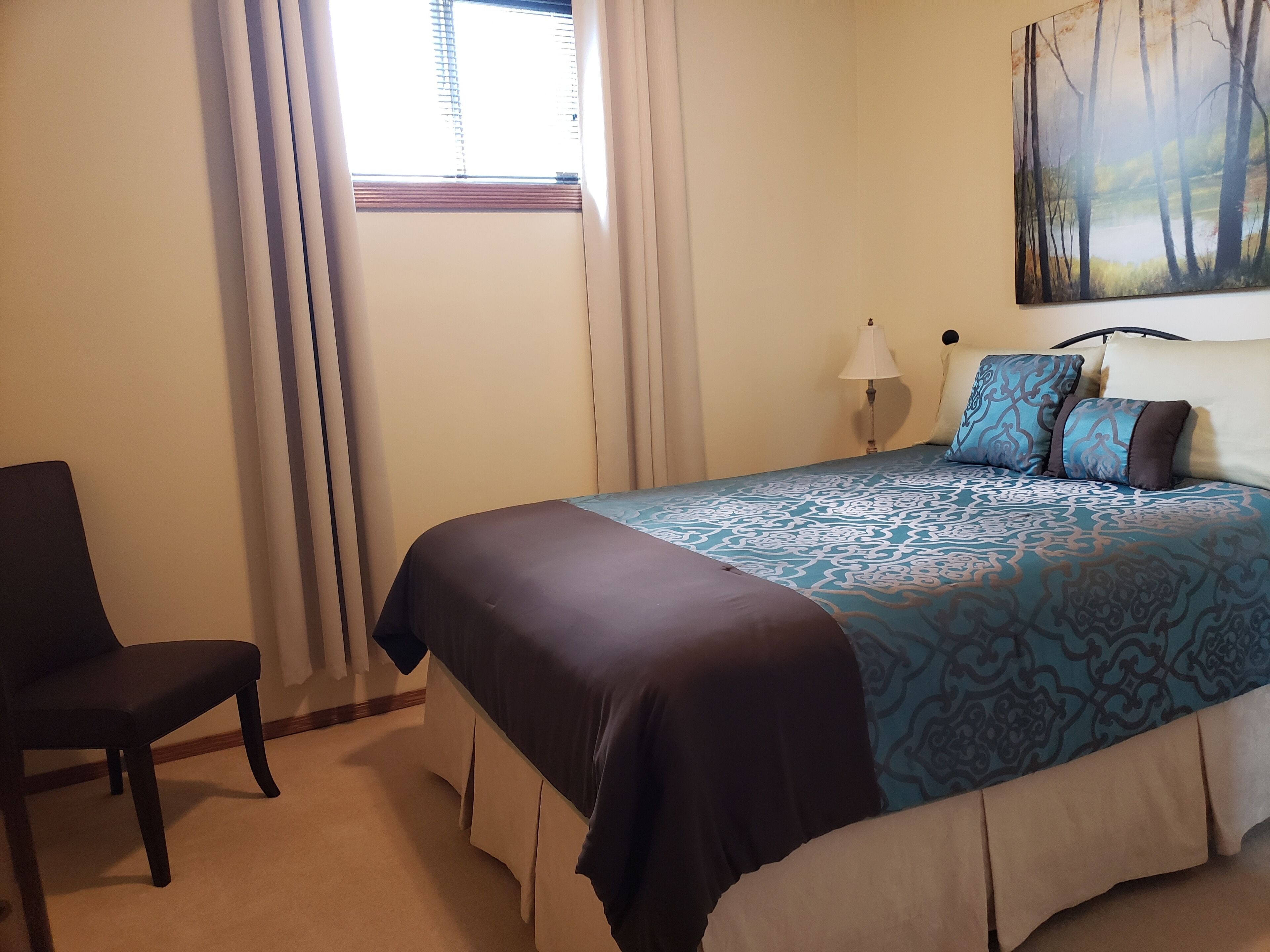 A bedroom with a bed, a chair, a lamp, and a painting on the wall.