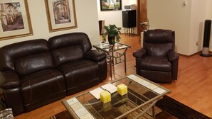 A living room with a brown leather sofa, a glass coffee table with candles, and a wooden floor. - PRIVATE 1 B/R Suite in Upscale formerShowhome  . 4 MIN walk to Lakeside beach Pk (Chestermere)