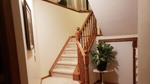 A carpeted staircase with wooden railings and a potted plant on a small table at the bottom. - PRIVATE 1 B/R Suite in Upscale formerShowhome  . 4 MIN walk to Lakeside beach Pk (Chestermere)