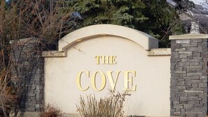 A sign with "THE COVE" in gold lettering on a beige wall, surrounded by stone walls and greenery. - PRIVATE 1 B/R Suite in Upscale formerShowhome  . 4 MIN walk to Lakeside beach Pk (Chestermere)