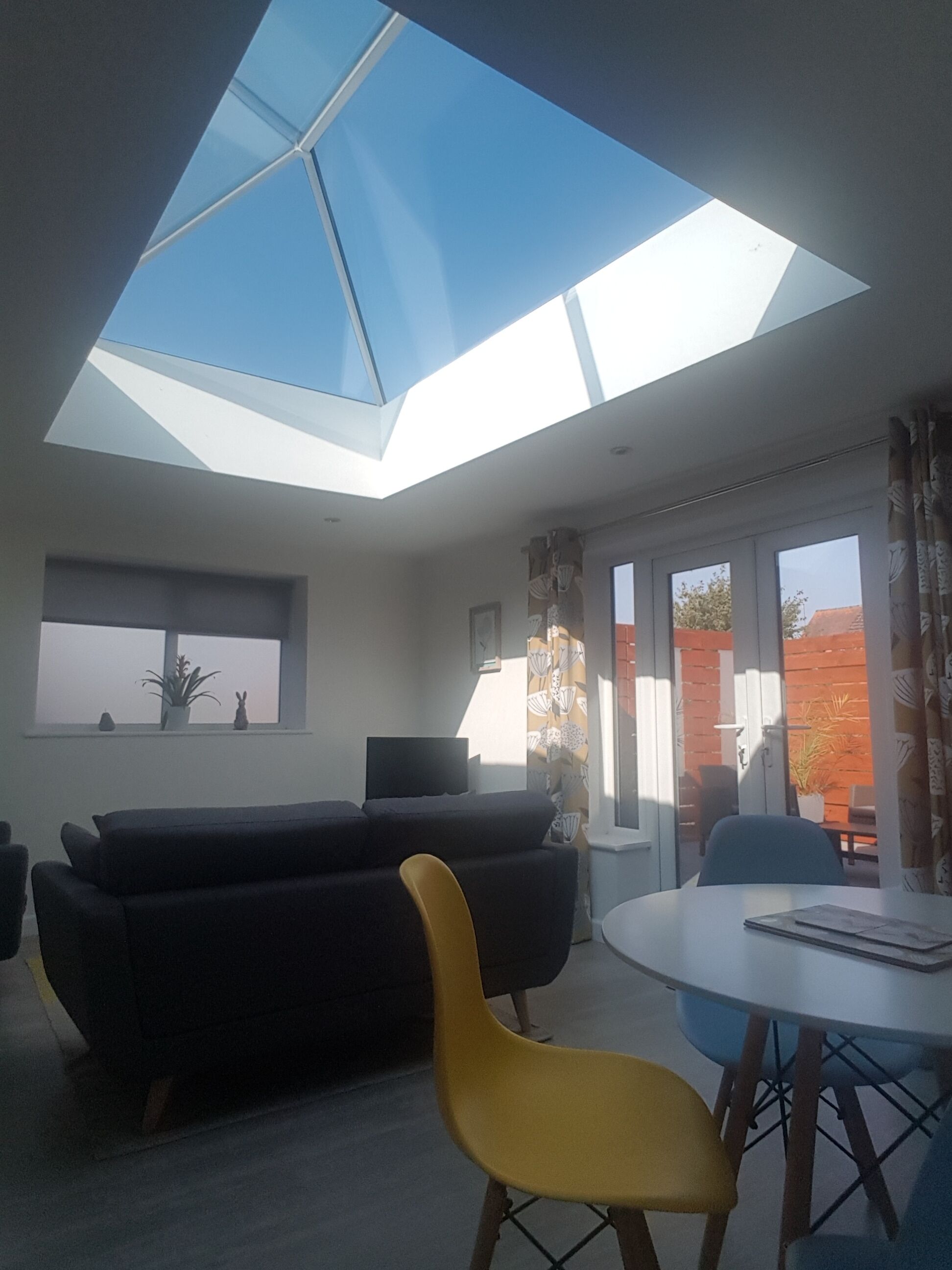 Een moderne woonkamer met dakraam, een bank, een gele fauteuil, een televisie en een eettafel.