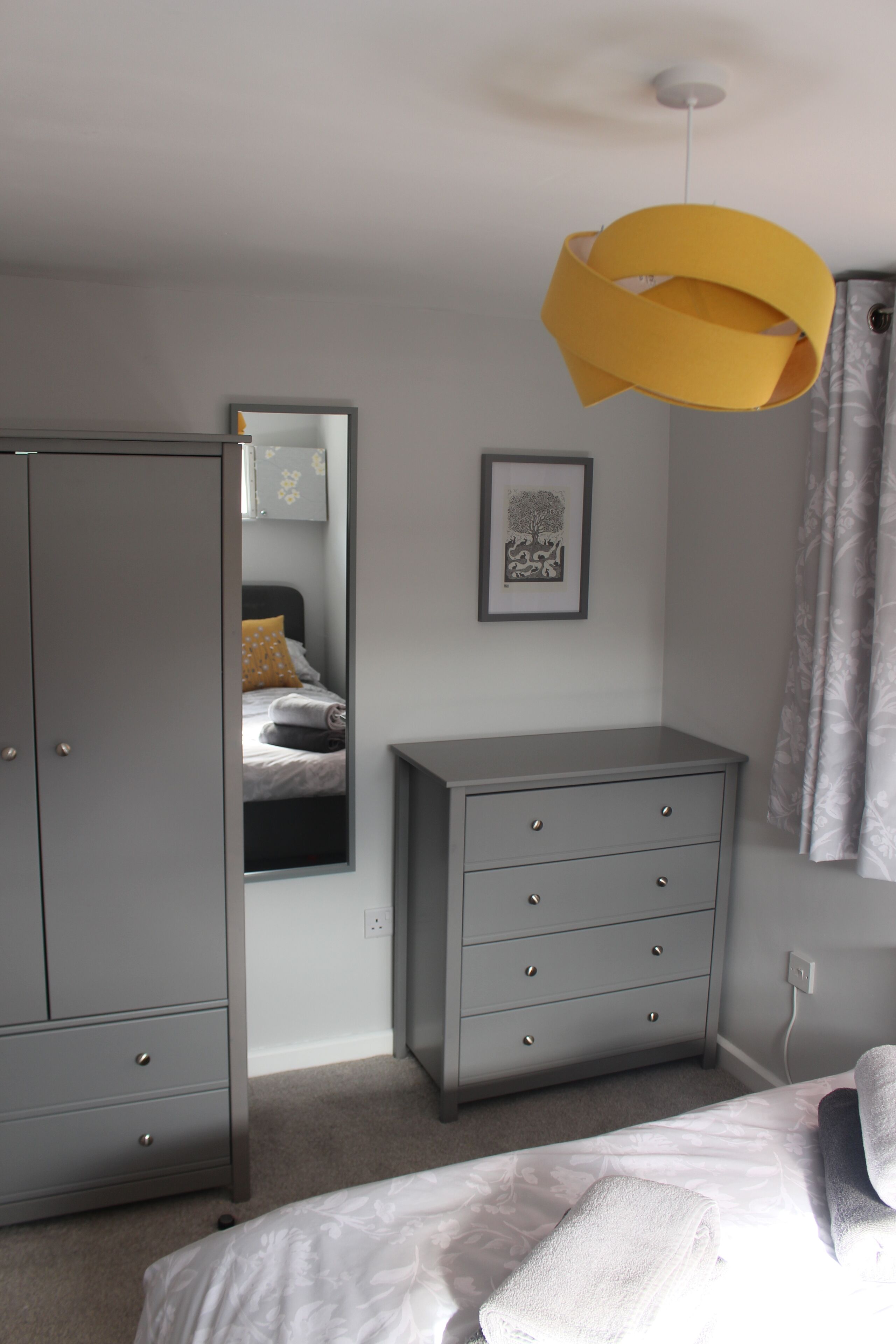 Un dormitorio con cama, armario, cómoda, espejo y lámpara colgante.