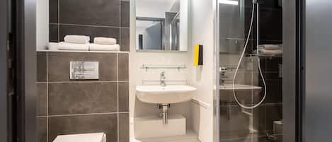 Un baño moderno con inodoro, lavamanos y ducha con mampara de vidrio.