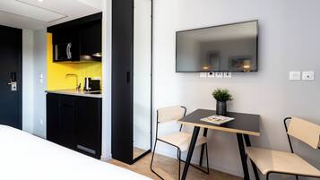 A modern kitchen with black cabinets, a yellow backsplash, and a black dishwasher. There is a dining area with a table, two chairs, and a flat-screen TV mounted on the wall.