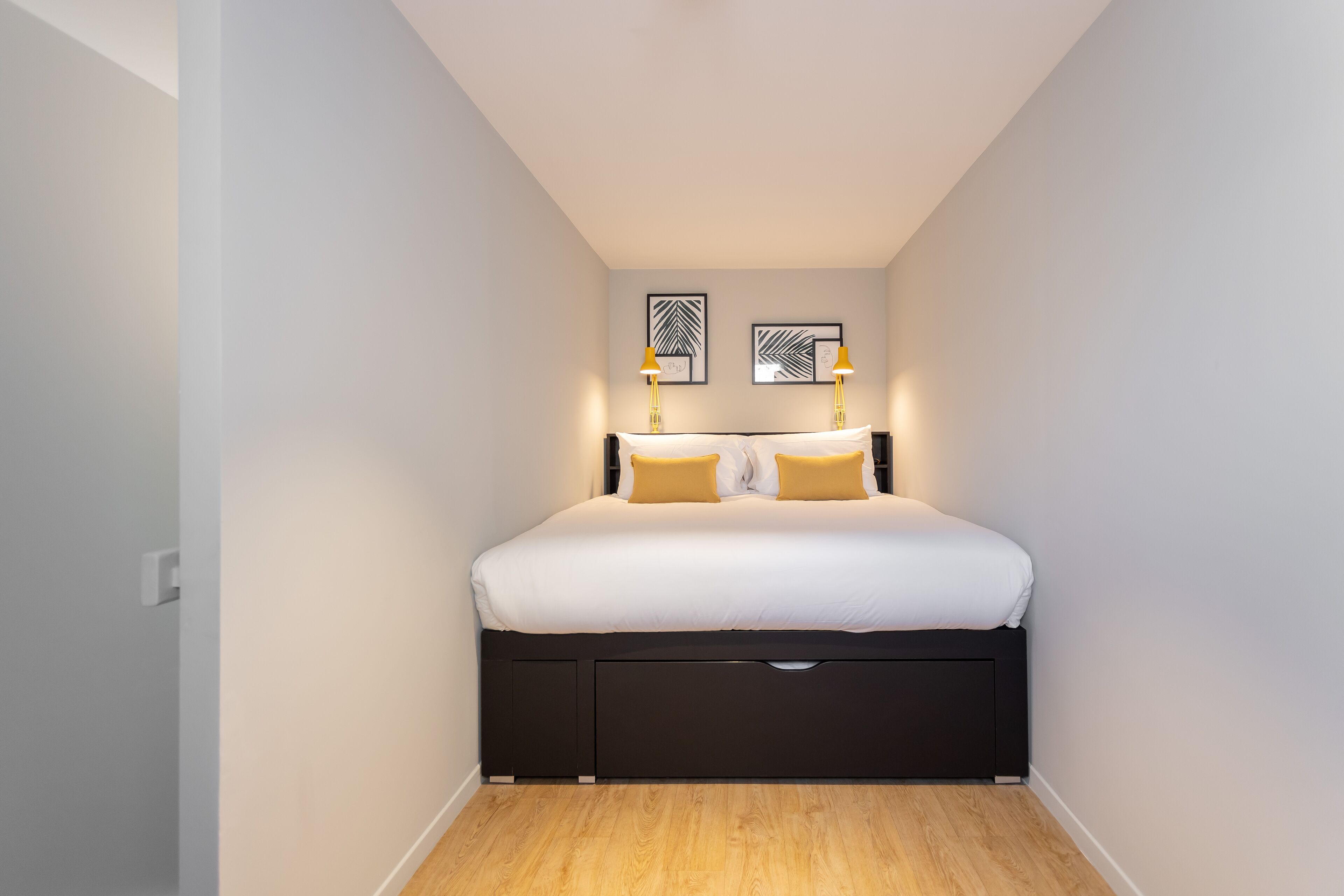 A bedroom with a bed, two wall-mounted lamps, and two framed artworks.