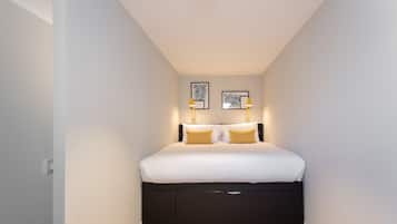A bedroom with a bed, two wall-mounted lamps, and two framed artworks.