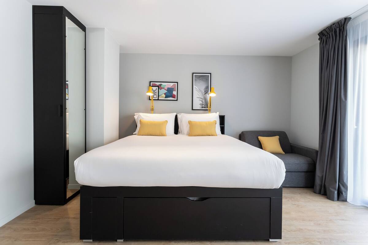 Ein modernes Schlafzimmer mit einem großen Bett, zwei Nachttischen mit Lampen, einem grauen Sofa und einem Kleiderschrank.
