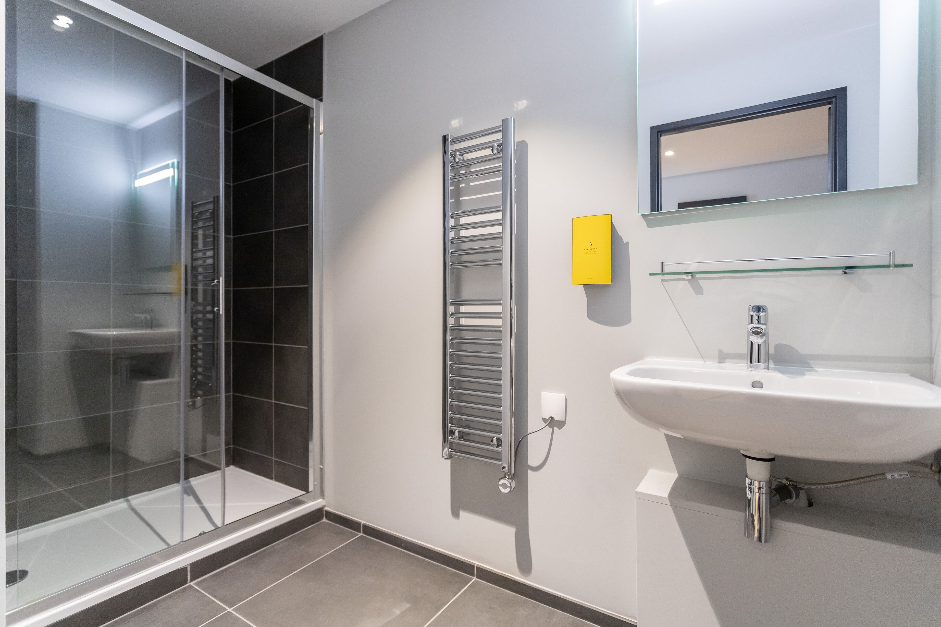 Un baño moderno con cabina de ducha de vidrio, toallero de pared, lavabo y espejo.