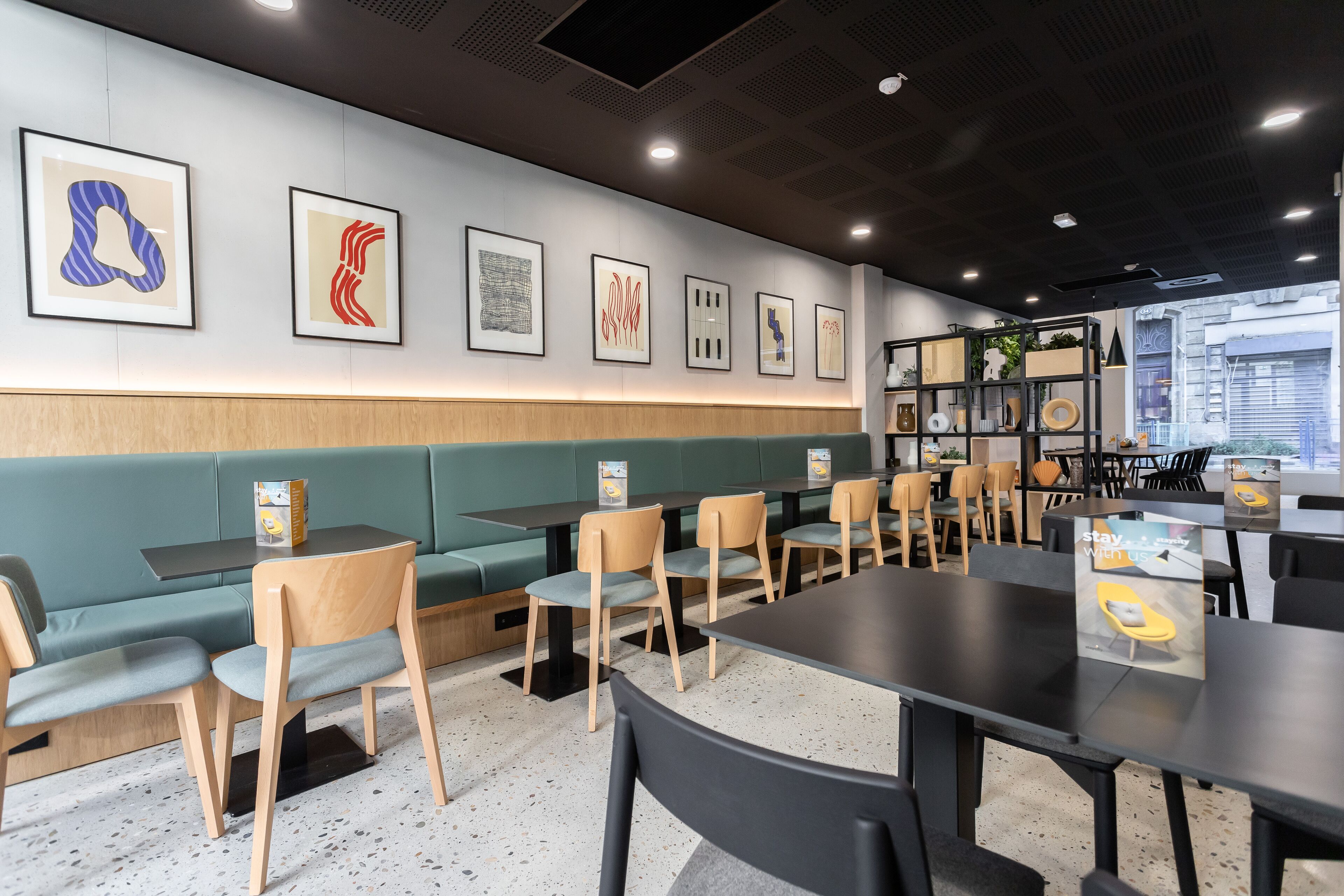 Een modern restaurantinterieur met groene banken, houten stoelen en zwarte tafels.