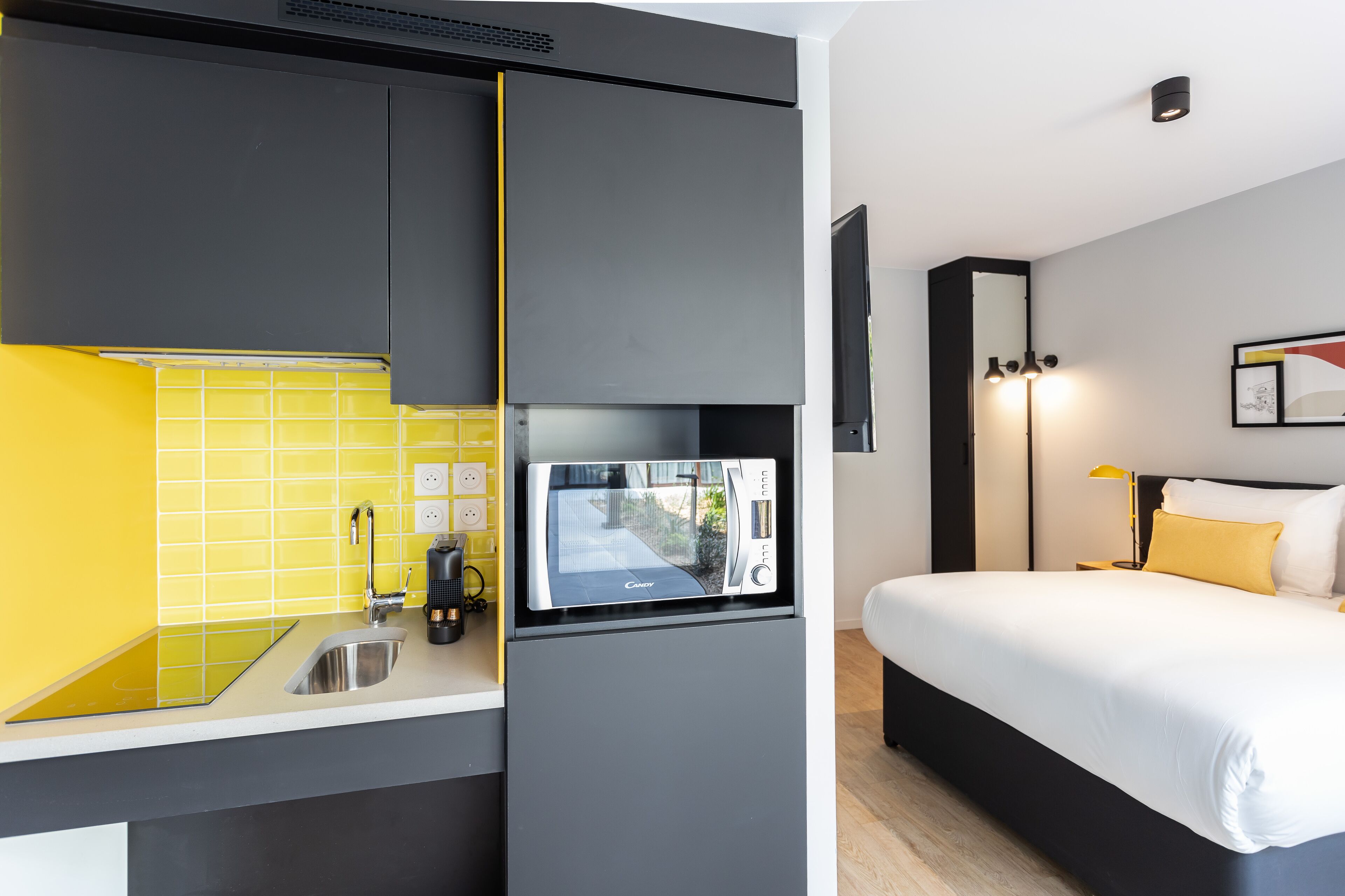 Una habitación de hotel compacta con kitchenette, una cama y una mesita de noche.