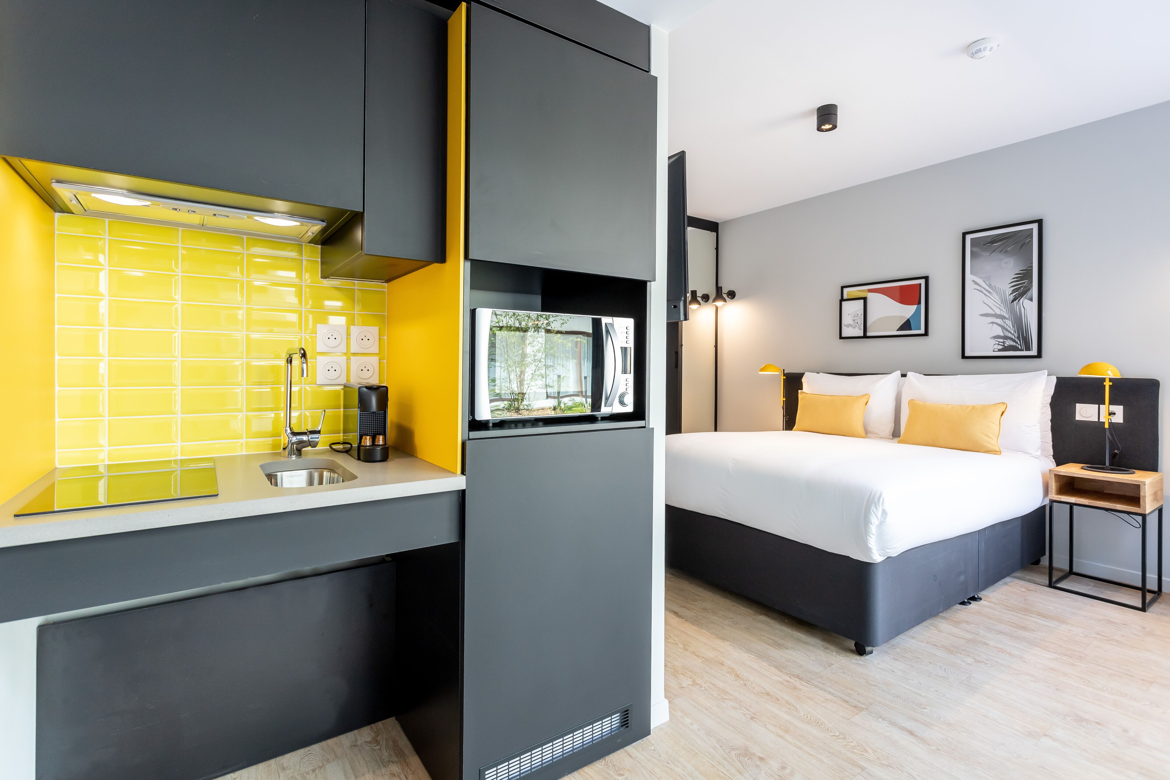 Habitación compacta con kitchenette, una cama con dos almohadas y una mesita de noche con lámpara.
