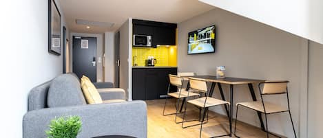 Un espacio habitable moderno y funcional, con kitchenette, zona de comedor con mesa y sillas, y área de estar con sofá y una mesita de centro.