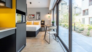 Una habitación de hotel moderna con una cama, una mesita, una silla y un amplio ventanal con vistas a la ciudad.