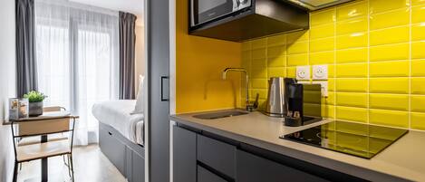 A compact kitchen with a microwave, kettle, and yellow-tiled backsplash.