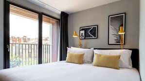 Habitación de hotel con una cama grande, dos lámparas de noche y vistas a edificios a través de la ventana.