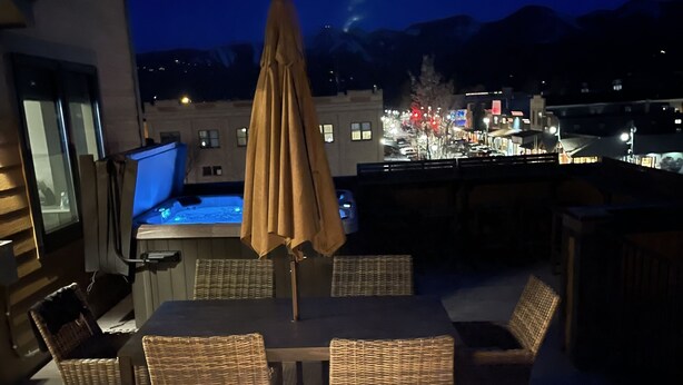 A rooftop patio with a table and chairs, a laptop, and a lit fireplace.