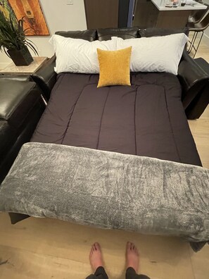 A bed with a dark brown mattress, a white pillow, and a mustard-colored pillow. There is a gray blanket on the floor. - Luxury Whitefish Penthouse w/Hot Tub on Central Ave (Whitefish)