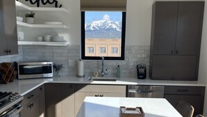 A modern kitchen with a large island, a view of a mountain through a window, and a 'Father' sign on the wall.