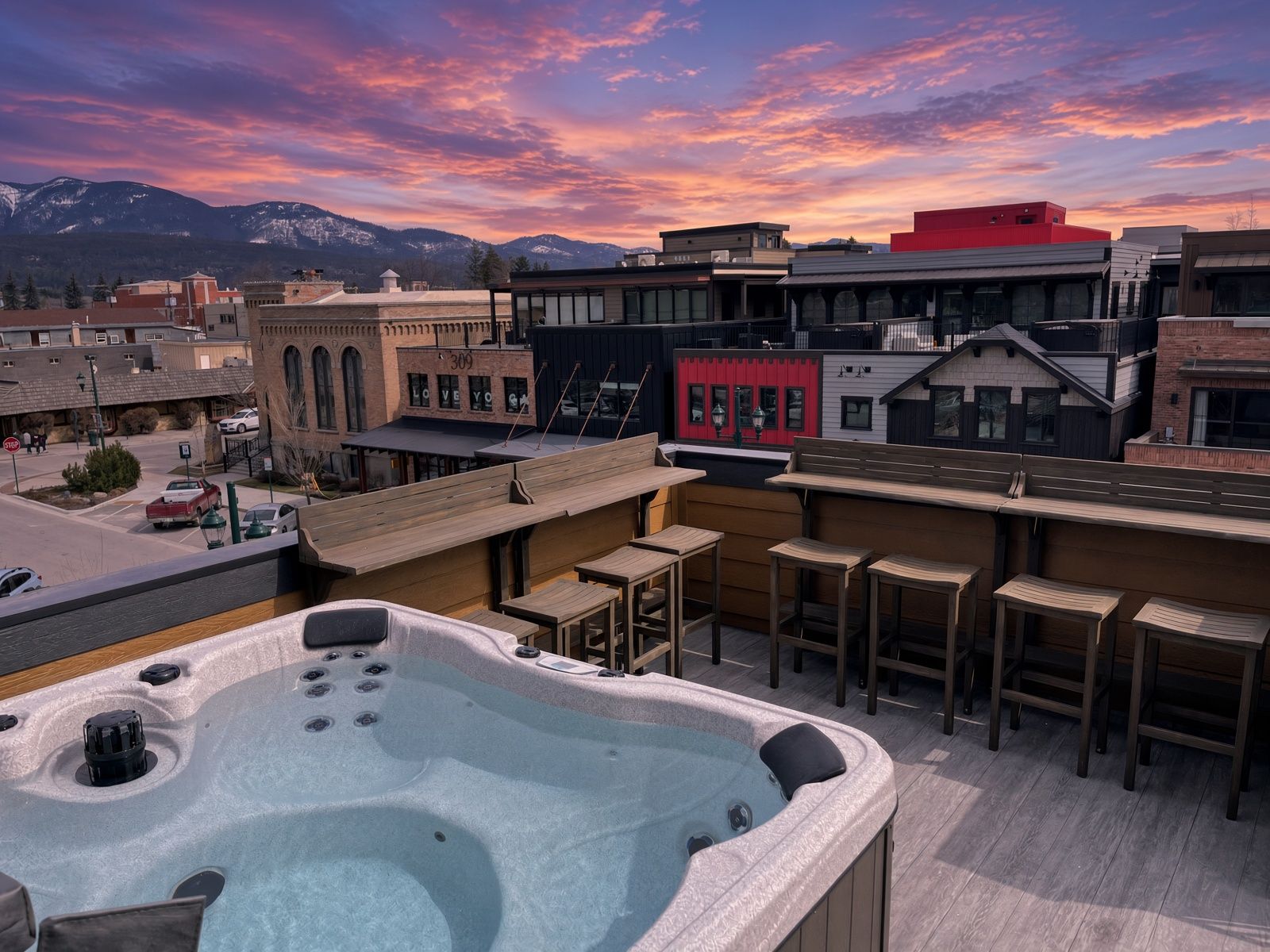 Een terras op het dak met een hottub, zitplaatsen en uitzicht op een stad met gebouwen en bergen op de achtergrond.