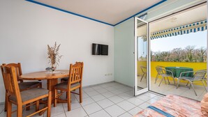 Una stanza con un tavolo da pranzo, sedie, una TV e un'ampia vetrata scorrevole che dà su uno spazio esterno con sedie e un tavolo.