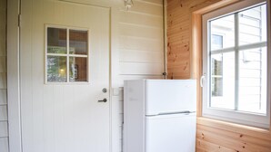 En vit dörr med ett litet fönster, ett vitt kylskåp och en vägg av trä med ett fönster.