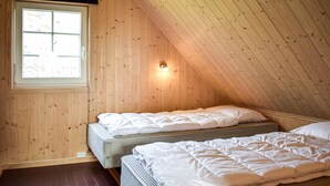 Ett litet, ombonat sovrum på vinden med träväggar, ett sluttande tak och ett fönster som släpper in naturligt ljus.