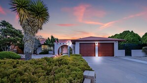 A modern house with a red garage, surrounded by well-maintained landscaping and a tall palm tree. - Relaxing, comfortable home for entertaining or enjoying the view (Rio Rancho)