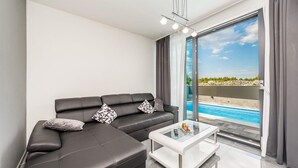 A modern living room with a black leather sofa, a glass coffee table, and a view of a swimming pool through a sliding glass door.