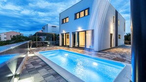A modern house with a swimming pool, a covered outdoor seating area, and a large water feature.