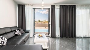 A modern living room with a black leather sofa, a glass coffee table, and a view of a swimming pool through a glass door.