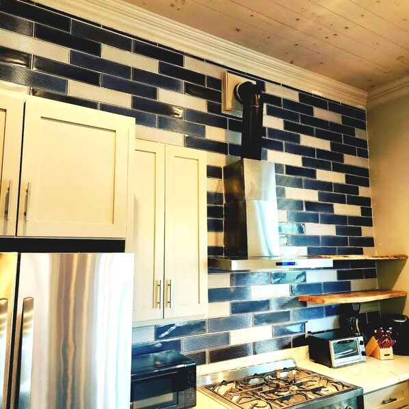 Una cocina con armarios blancos, un refrigerador de acero inoxidable, un microondas negro, una estufa a gas y un salpicadero de azulejos.