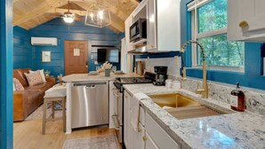 A modern kitchen with a central island, stainless steel appliances, and a large window. - Pops Lookout Mountain Luxury Tiny Cabin with Spa (Chattanooga)
