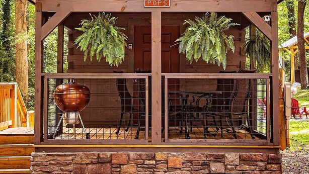 A wooden cabin with a stone foundation, a covered patio with outdoor seating, and a sign reading 'POPS'. - Pops Lookout Mountain Luxury Tiny Cabin with Spa (Chattanooga)