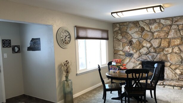 A dining area with a stone wall, a clock, and a window with blinds.