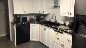 A modern kitchen with white cabinets, a black countertop, a built-in dishwasher, a refrigerator, and a coffee maker.