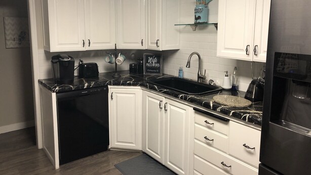 A modern kitchen with white cabinets, a black countertop, a built-in dishwasher, a refrigerator, and a coffee maker.