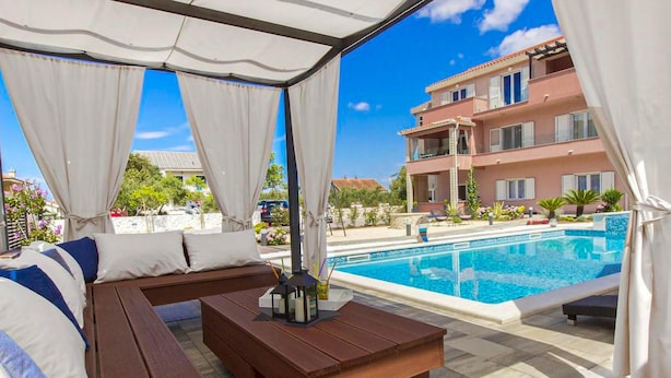 A covered outdoor seating area with a pool and a building in the background.