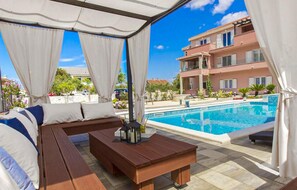 A covered outdoor seating area with a pool and a building in the background. - 3 bedroom cozy apartment in Grebastica (Grebastica)